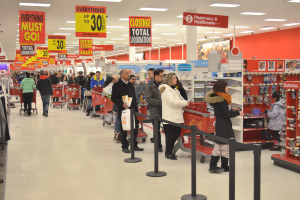 Ein überfüllter Walmart-Laden mit Einkaufstaschen tragenden Kunden und Einkaufswagen, umgeben von Warenregalen, Informationsschildern und Deckenleuchten, wahrscheinlich während eines Black Friday-Verkaufs.