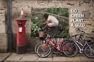 Mehrere Fahrr√§der sind in der N√§he einer Briefkasten mit einem Sicherheitstonne darauf geparkt, mit einem Plakat an einer Wand im Hintergrund und einem Weg am unteren Rand des Bildes.