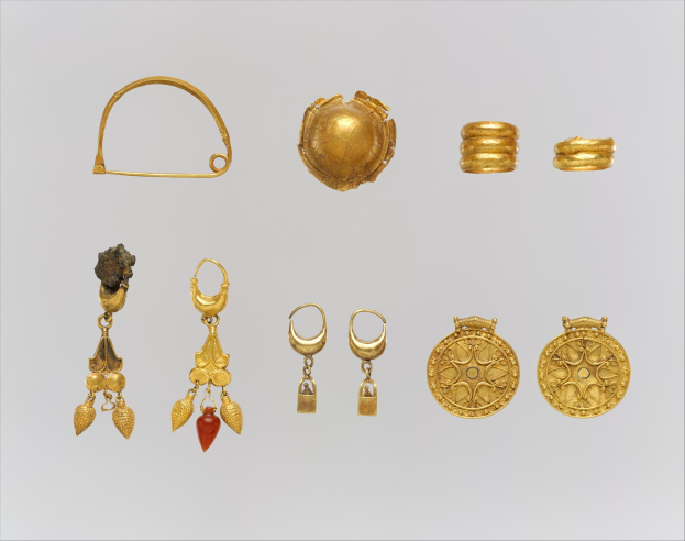Eine Sammlung von goldenen Ohrringen und Ringen, die auf einer weißen Oberfläche angeordnet sind und im goldenen Licht funkeln.