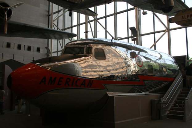 Ein Flugzeug der American Airlines wird in einem Museum ausgestellt, umgeben von Menschen, mit einer Treppe auf der rechten Seite und einem Gebäude, Bäumen und einem klaren blauen Himmel im Hintergrund.