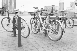 Mehrere Fahrräder auf einer Fläche mit Gebäuden im Hintergrund, in Schwarz-Weiß dargestellt.