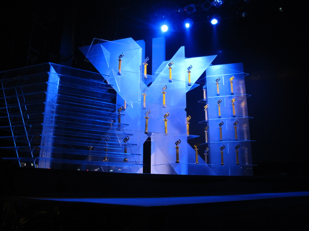 Eine Bühne für eine Preisverleihung mit dunklem Hintergrund, beleuchtet von ein paar Lichtern und mit ein paar Gegenständen, die mit dem Ereignis in Verbindung stehen.