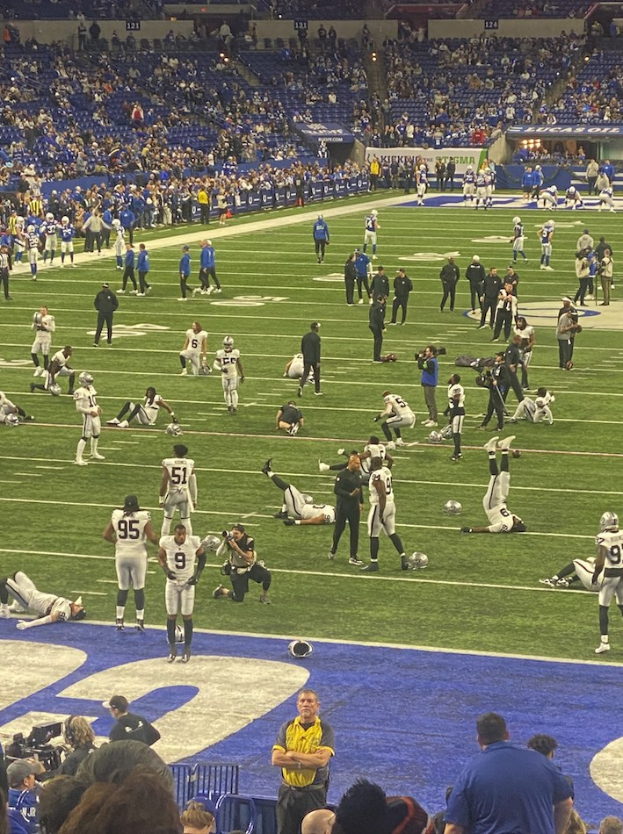 Ein Fußballspiel in einem Stadion mit Menschen im Stehen und Sitzen im Hintergrund und einer Person mit einer Kamera, die das Ereignis überträgt.
