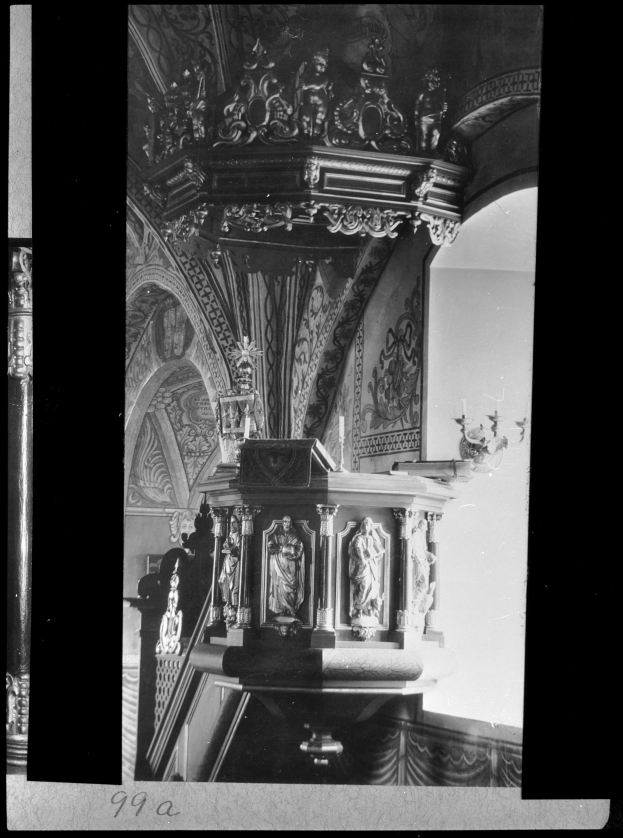 Ein Schwarz-Weiß-Foto eines Kirchenpults mit geschnitzten Säulen und einer texturierten Wand im Hintergrund, mit Text am unteren Rand.