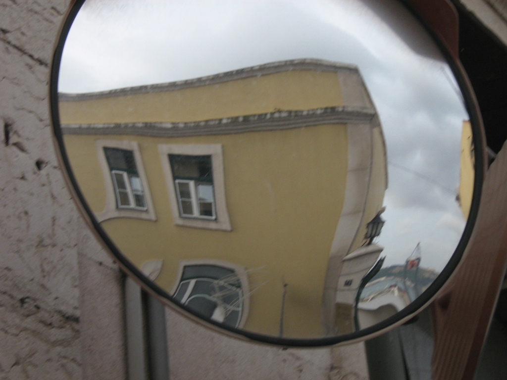 Ein Straßenverkehrsspiegel, der Gebäude, Lichter und den Himmel reflektiert, mit einer Wand im Hintergrund.