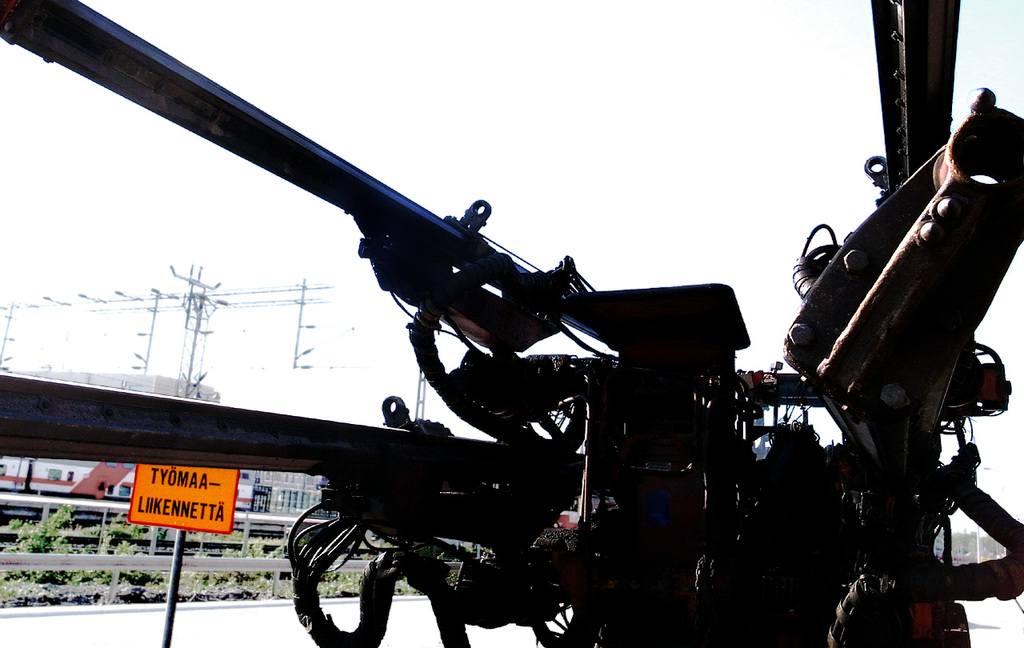 Eine Maschine ist im Vordergrund mit Strommasten, Kabeln, Barrieren, Pflanzen und Himmel im Hintergrund.