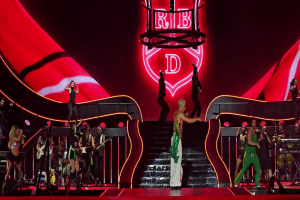 Eine Gruppe von Menschen auf einer Bühne, einige halten Musikinstrumente, mit Stufen, die zur Bühne führen, und einem Schild im Hintergrund mit der Aufschrift 'Rihanna - Live in der O2 Arena, London'.