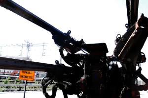 Eine Maschine ist im Vordergrund mit Strommasten, Kabeln, Absperrungen, Pflanzen und Himmel im Hintergrund.