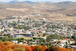 Eine Landschaft mit Häusern, Bäumen, Stromleitungen, Hügeln und einem klaren Himmel.