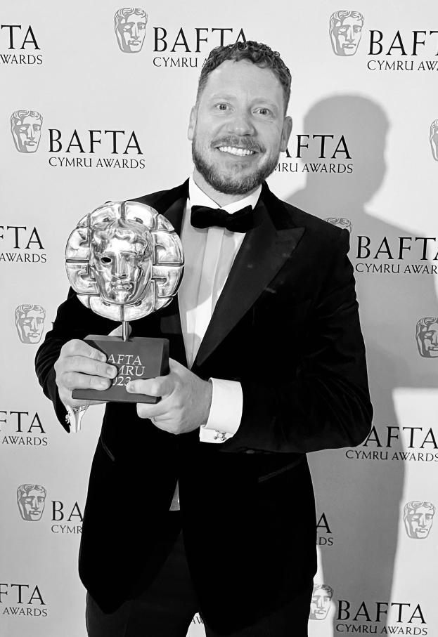 Ein Mann im Smoking, der eine BAFTA-Auszeichnung hält und lächelt, mit einem Hintergrundplakat, auf dem "BAFTA Awards 2018" steht