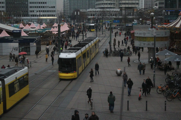 Eine belebte Stadtstraße mit Fußgängern, Radfahrern, Regenschirmen, Straßenlaternen, Zelten, Gebäuden, Bäumen und einem klaren blauen Himmel.