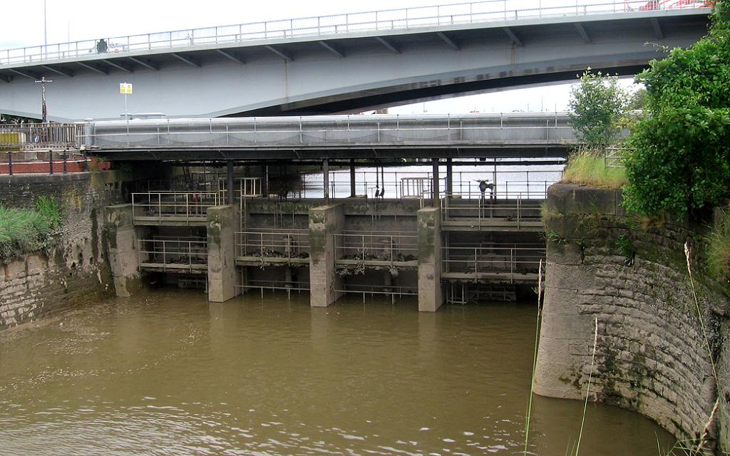 Ein Blick auf die Dammtore mit fließendem Wasser, eine Brücke und umliegende Bäume und Pflanzen.