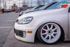 Autos auf einer Straße mit einem unscharfen Hintergrund von Bäumen, Gebäuden und Himmel und einem Logo in der rechten oberen Ecke.