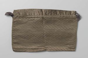 Ein kleiner grüner Stoffbeutel mit schwarzen Punkten, mit einer Zugschnur als Verschluss, auf einer weißen Oberfläche.