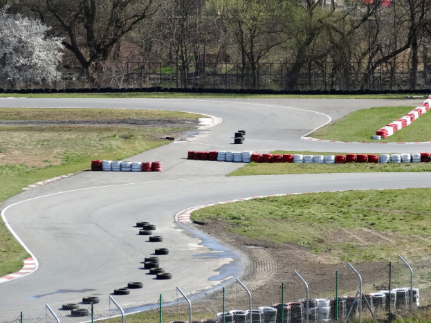 Rennstrecke mit zahlreichen Reifen entlang ihrer Kanten, von Gras und Maschendrahtzaun umgeben, mit Bäumen im Hintergrund.