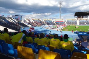 Ein voller Stadion mit Zuschauern bei einem Fußballspiel, mit Bannern, Anzeigetafel, Metallrohrdach und bewölktem Himmel.