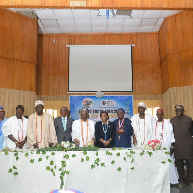 Gruppe von Menschen, die um einen weißen Tisch mit Blumen und Blättern auf der ICCI International Trade Fair 2019 stehen, mit einem Banner, Projektionsbildschirm und Deckenbeleuchtung im Hintergrund.