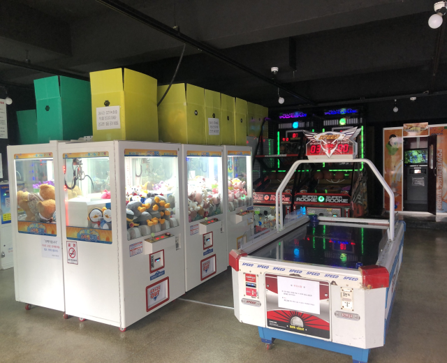 Ein vollgestellter Arcade-Raum mit verschiedenen Arcade-Spielen, einem Spielautomaten auf der rechten Seite, einem sichtbaren Boden und Deckenlampen.