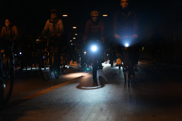 Eine Gruppe von Menschen, die nachts auf Fahrrädern eine Stadtstraße entlangfährt, trägt Helme und ist von Stadtlichtern beleuchtet.