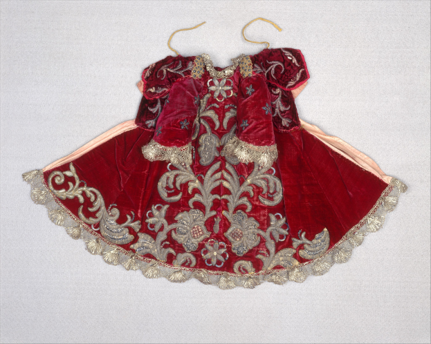 Ein rotes Samtkleid mit goldener Stickerei und detaillierten Designs, das an einem Bügel gegen einen weißen Hintergrund hängt.