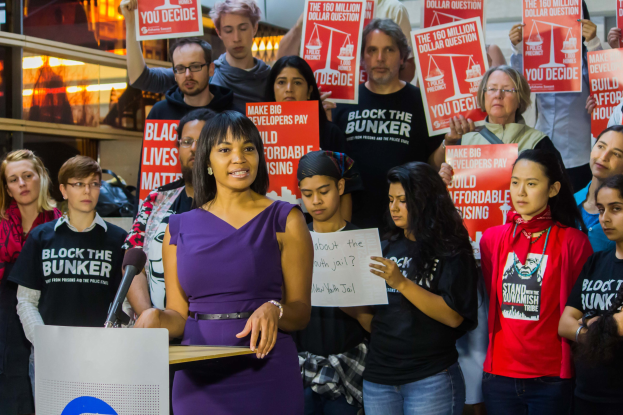 Eine Black-Lives-Matter-Aktivistin spricht auf einem Podium mit Mikrofon zu einer Menge mit Schildern.
